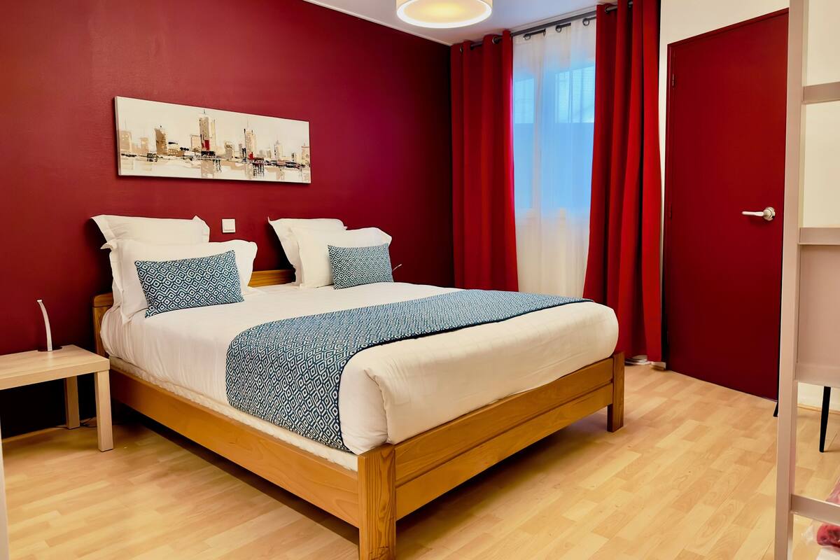 A neatly made bed with a patterned blanket and pillows, a wooden headboard, and a cityscape painting on the wall.