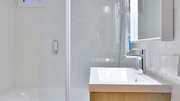 Ein modernes Badezimmer mit einer Glasdusche, einem weißen Waschbecken und einem Holz-Waschtisch.