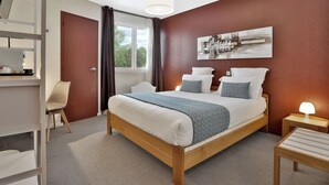 A neatly arranged bedroom with a bed, bedside table, and a desk area. - Hôtel Europa (Maussac)