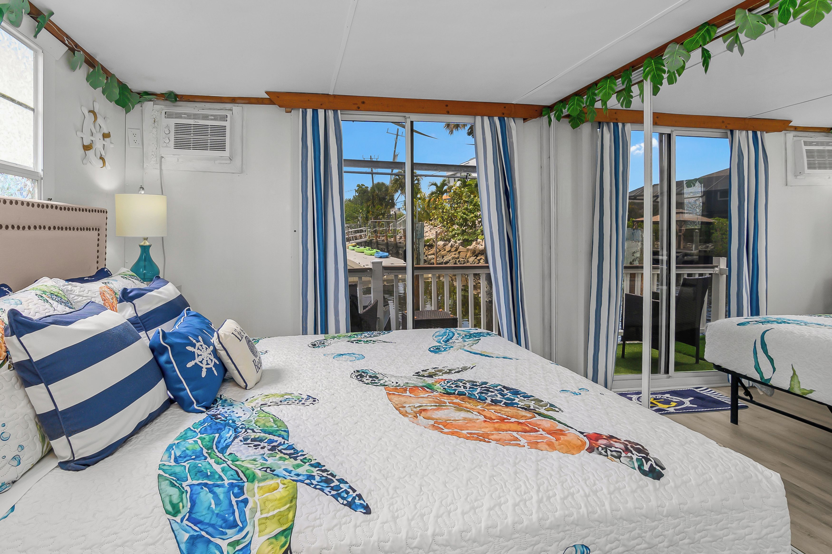 A bedroom with a bed, a nightstand, a lamp, and a view of the outdoors.