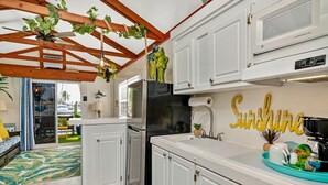 Une cuisine avec des meubles blancs, un réfrigérateur noir et un ventilateur de plafond.
