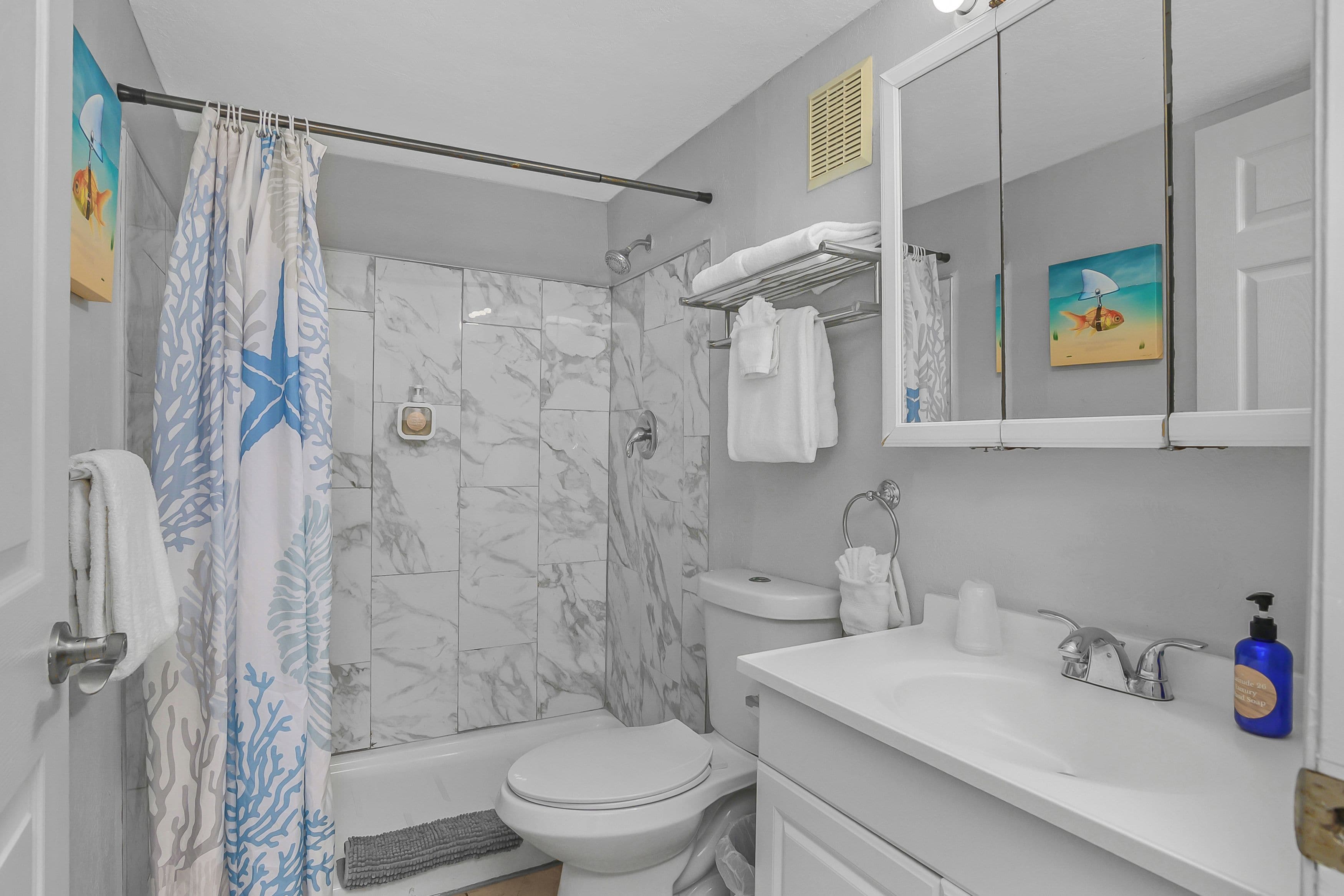 A bathroom with a shower curtain, a toilet, a sink with a soap dispenser, and a mirror.