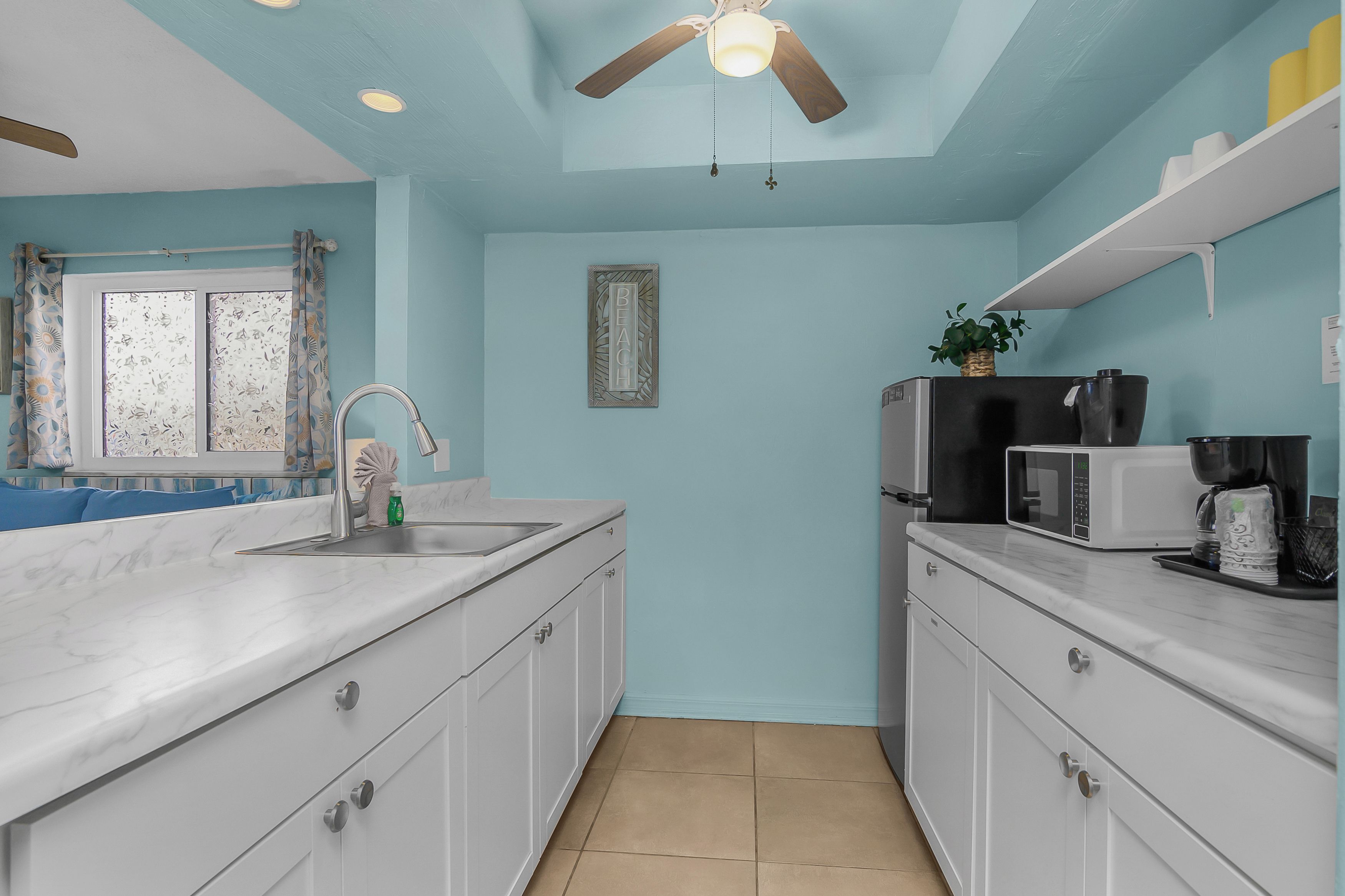 A kitchen with a ceiling fan, a sink, cabinets, a microwave, and a refrigerator.