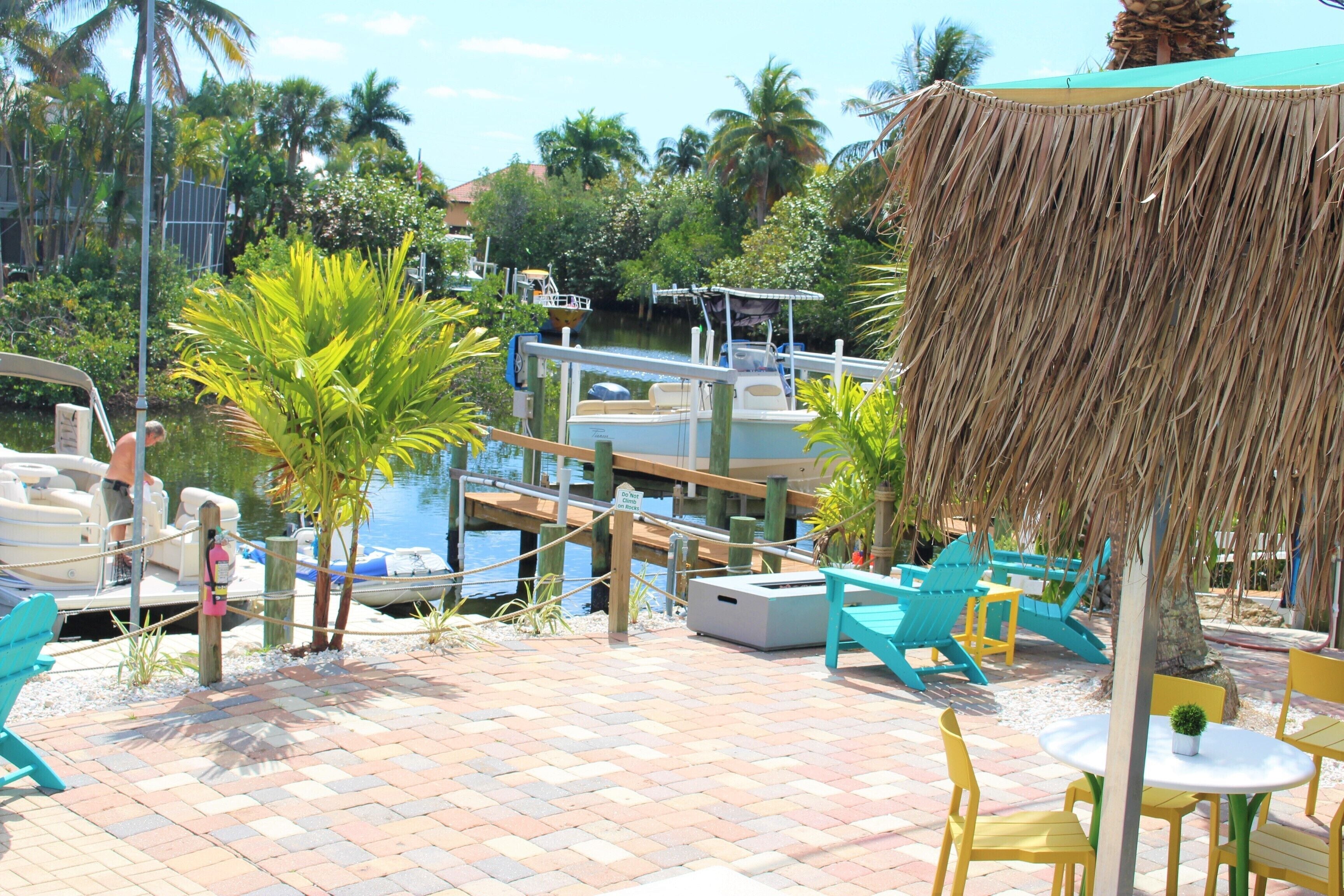 A tropical resort with a dock, lounge chairs, and a thatched umbrella.