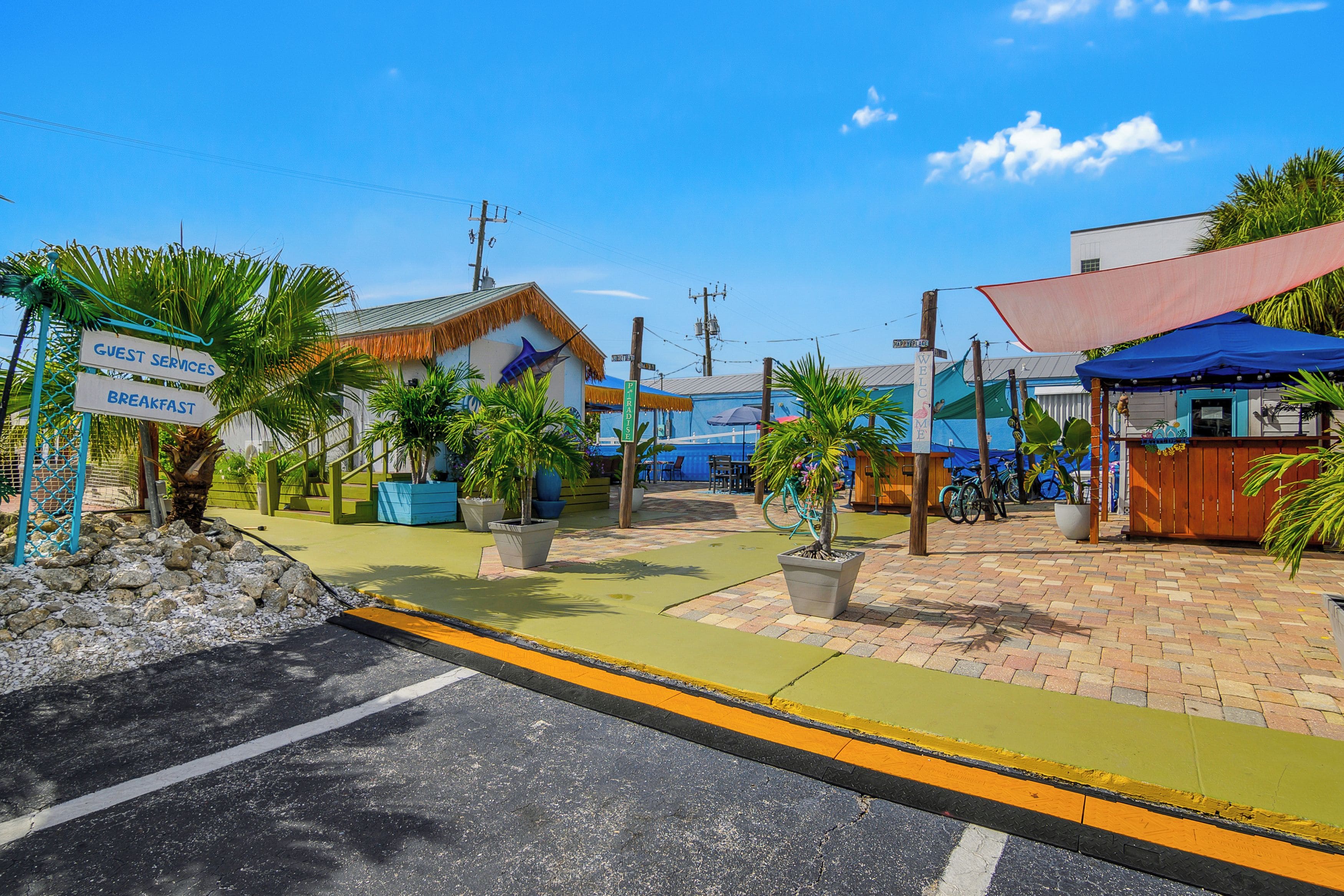 A tropical resort with a guest services sign, a welcome sign, and a restaurant named 'PIRADISE'.