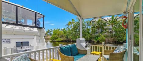 A covered outdoor seating area with wicker furniture and a view of a boat named 'CAROLINA DAZE' in the background.
