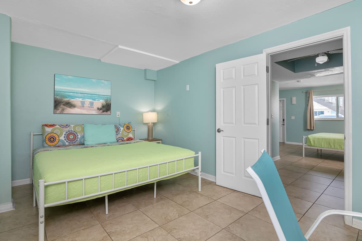 A bedroom with a bed, a chair, a door, and a painting on the wall.