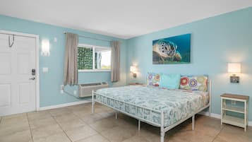 A bedroom with a bed, a window with curtains, a wall-mounted air conditioner, and a painting of a sea turtle.