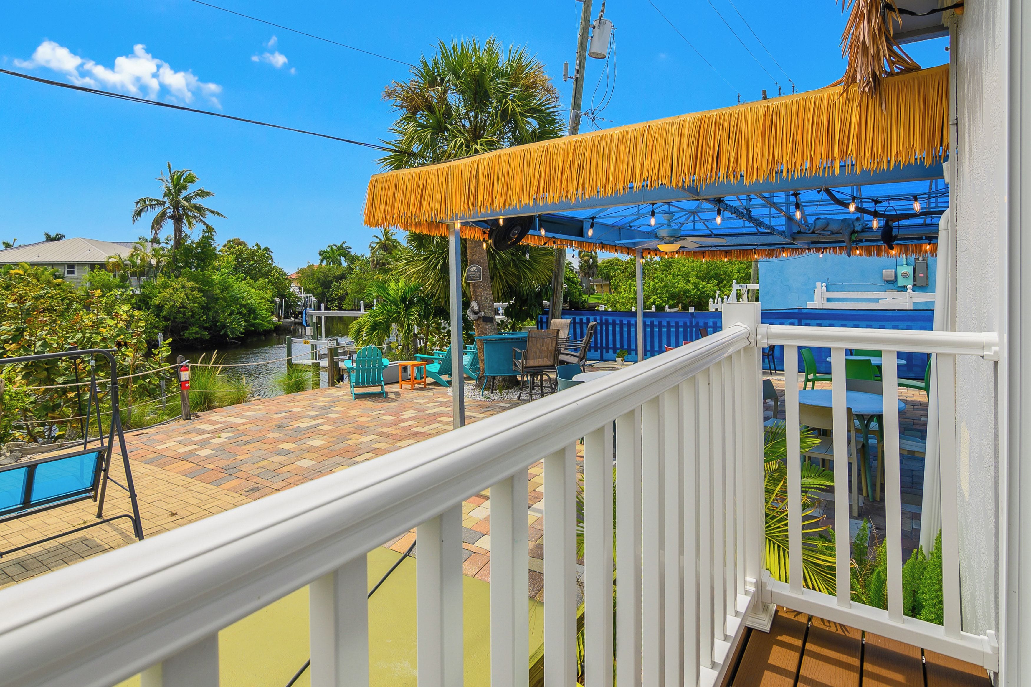 A balcony with a view of a pool, outdoor seating, and a tropical-themed awning.