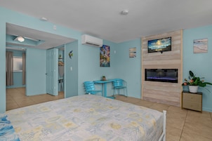 Quarto com uma cama, escrivaninha, duas cadeiras, televisão e planta em vaso.