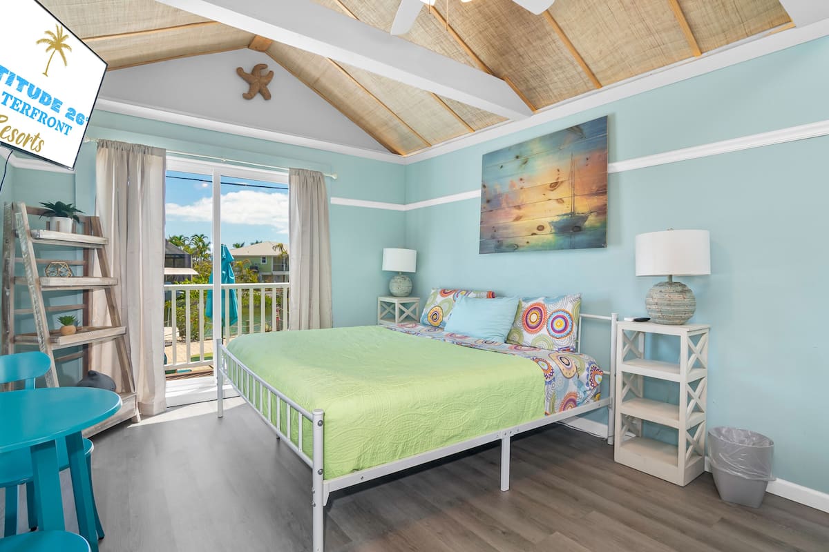 A bedroom with a bed, a desk, a chair, a window, and a view of the outdoors.