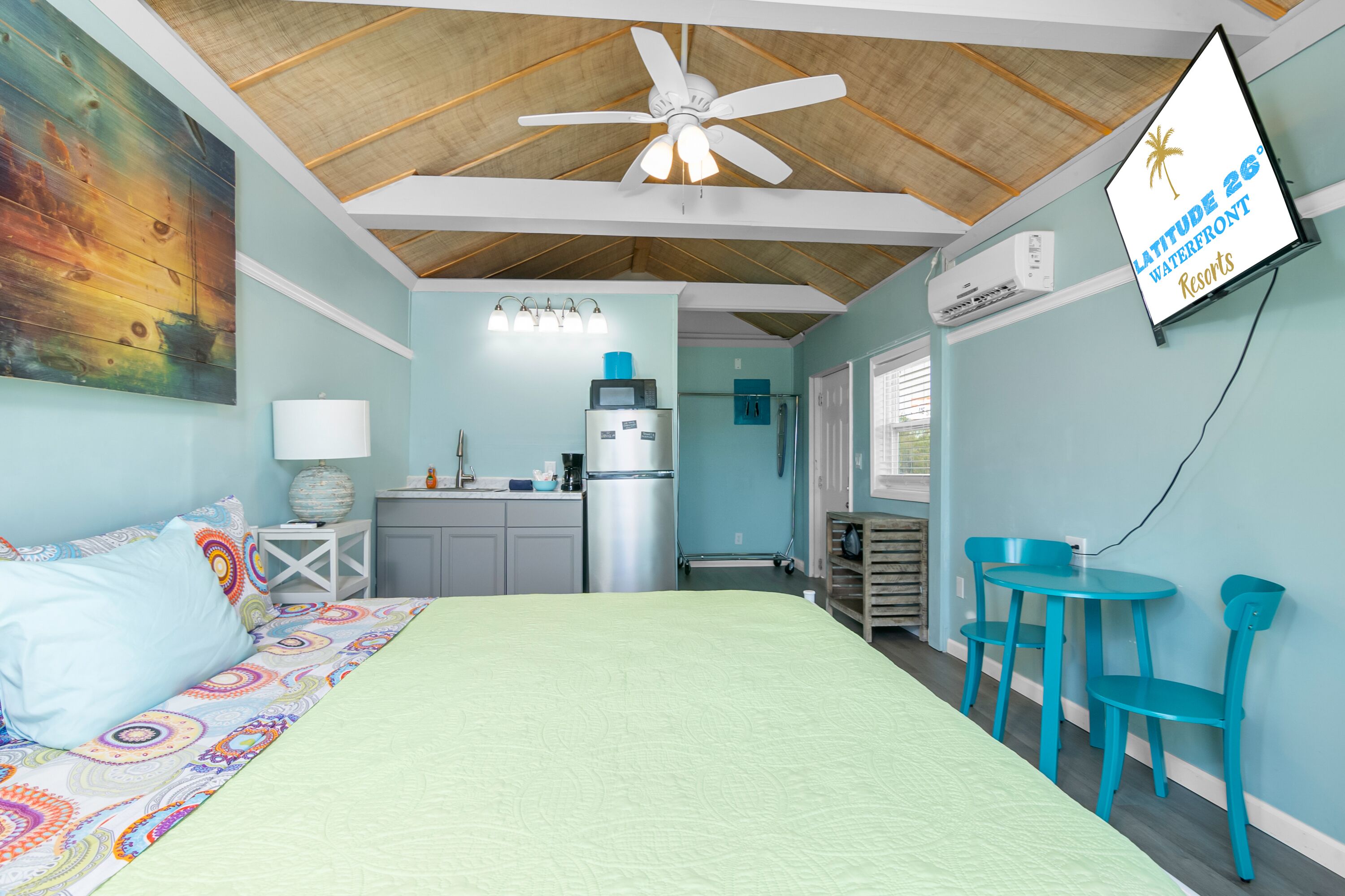Een kamer met een bed, een plafondventilator, een kitchenette en een bord dat de locatie aangeeft als Latitude 26° Waterfront Resorts.