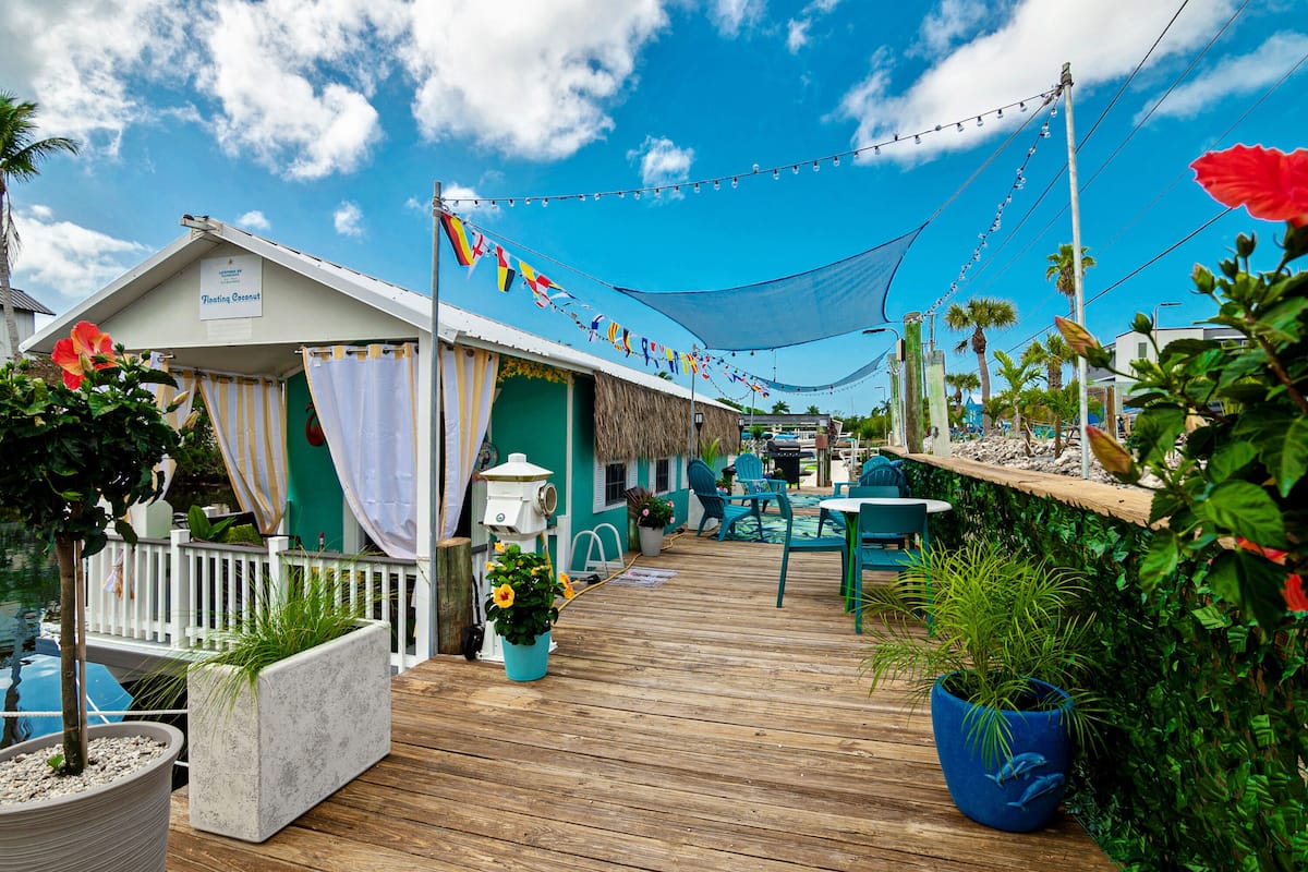 A wooden deck with potted plants, a thatched-roof structure, and string lights.