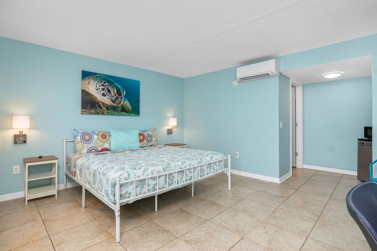 A bedroom with a bed, a nightstand, a wall-mounted air conditioner, and a door leading to another room.