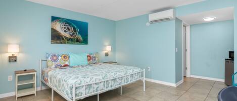 A bedroom with a bed, a nightstand, a wall-mounted air conditioner, and a door leading to another room.