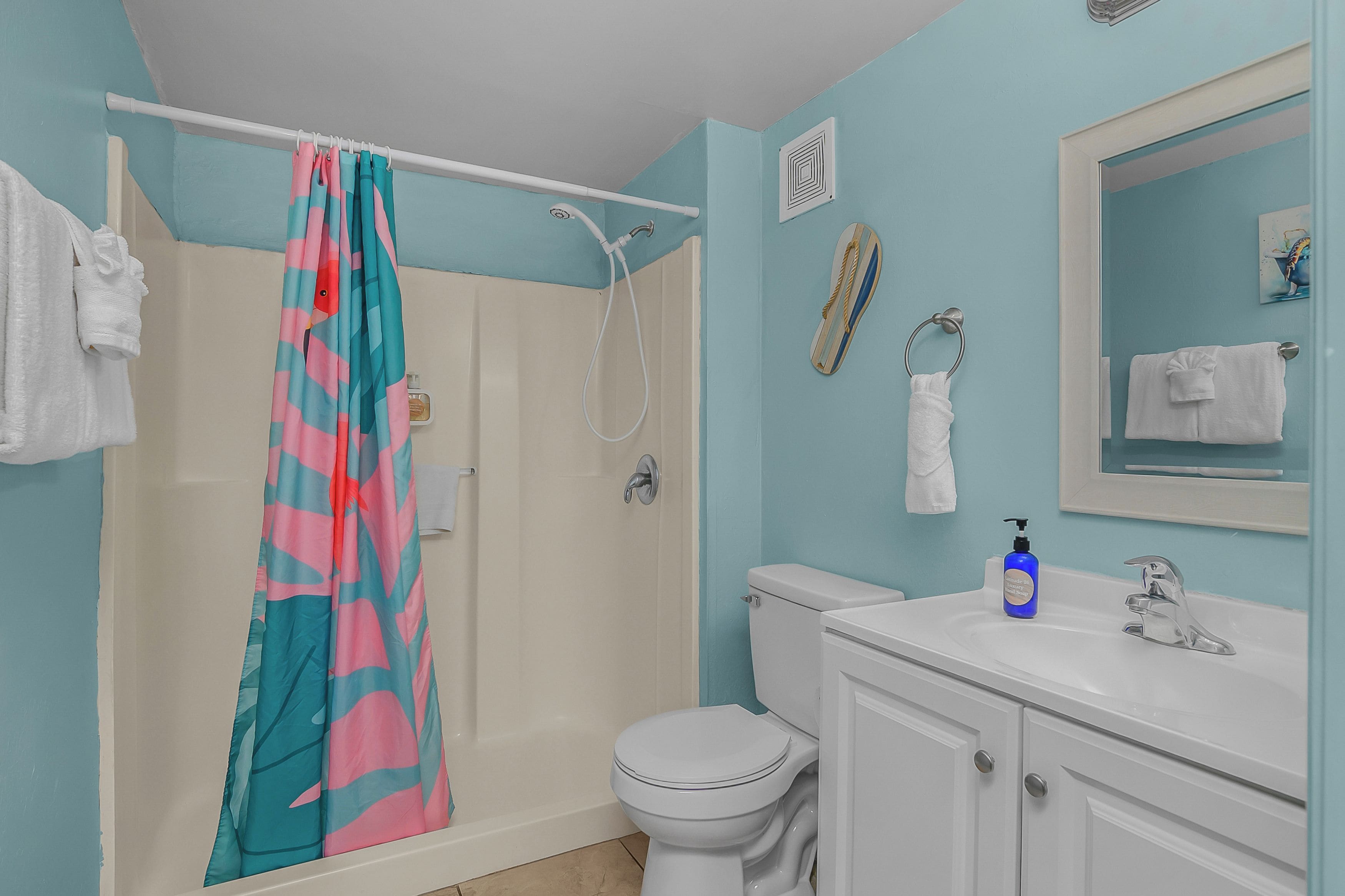 A bathroom with a shower curtain, a toilet, a sink with a soap dispenser, and a mirror.