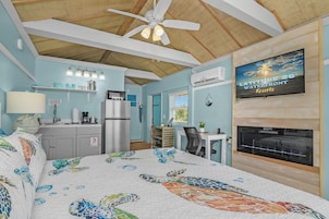 Ein Schlafzimmer mit Bett, Deckenventilator, einer Küchenzeile und einem an der Wand montierten Fernseher.