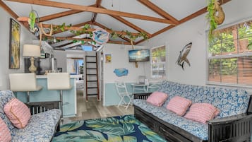 A room with a wooden ceiling, a sofa set, a dining area, and a TV displaying 'Latitude 26 Waterfront Resorts'.