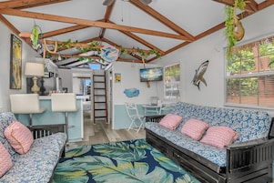 Habitación con techo de madera, un conjunto de sofás, zona de comedor y un televisor mostrando 'Latitude 26 Waterfront Resorts'.