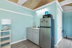 A kitchen with light blue walls, a stainless steel refrigerator, a sink, and a white shelf with a lamp. - Latitude 26 Waterfront Resort & Marina (Fort Myers Beach)