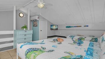 Une chambre à coucher comprenant un lit, une commode, un ventilateur de plafond, un téléviseur fixé au mur et une porte avec une pancarte.