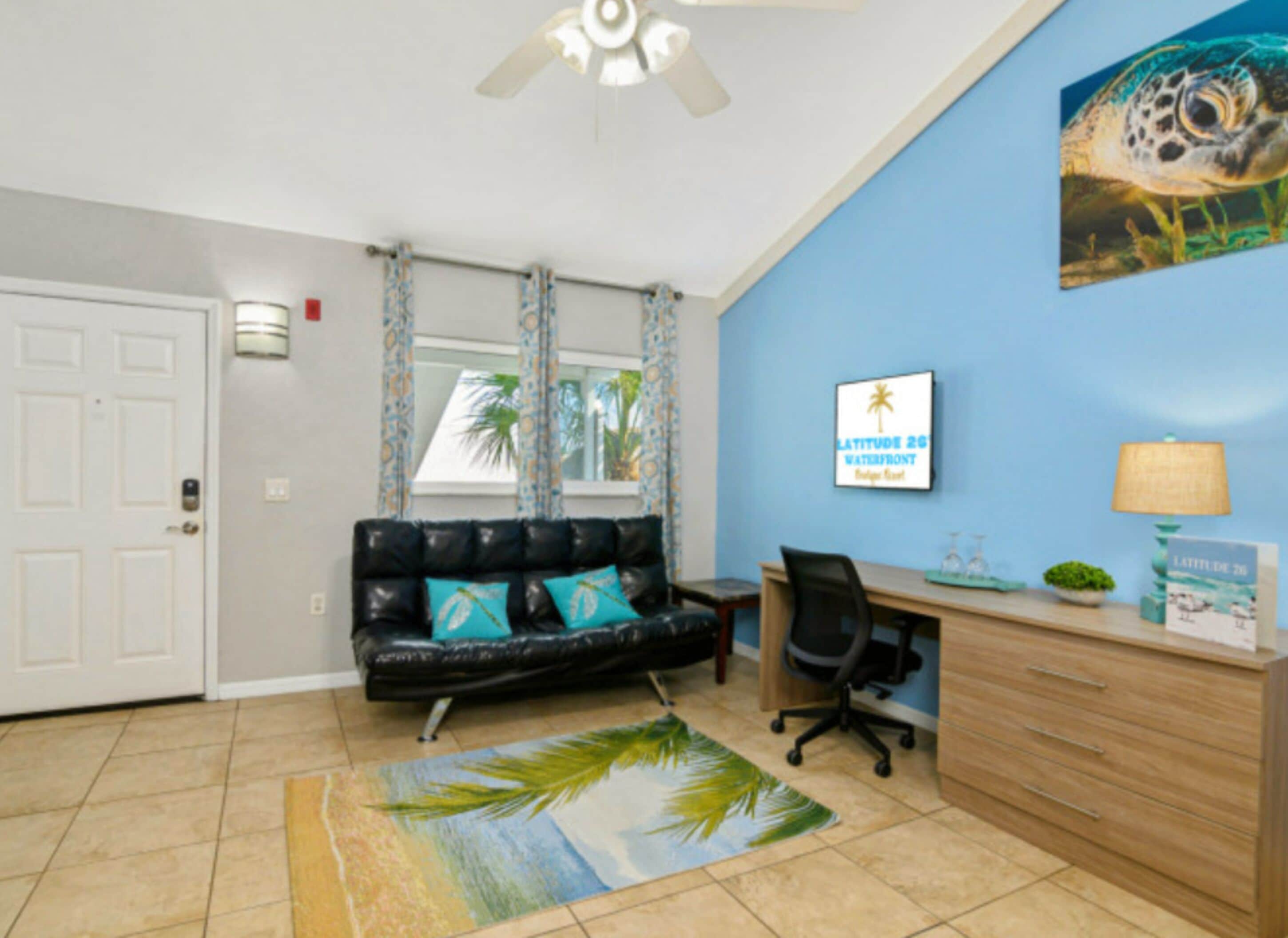 A room with a black leather sofa, a wooden desk, a computer, and a ceiling fan.