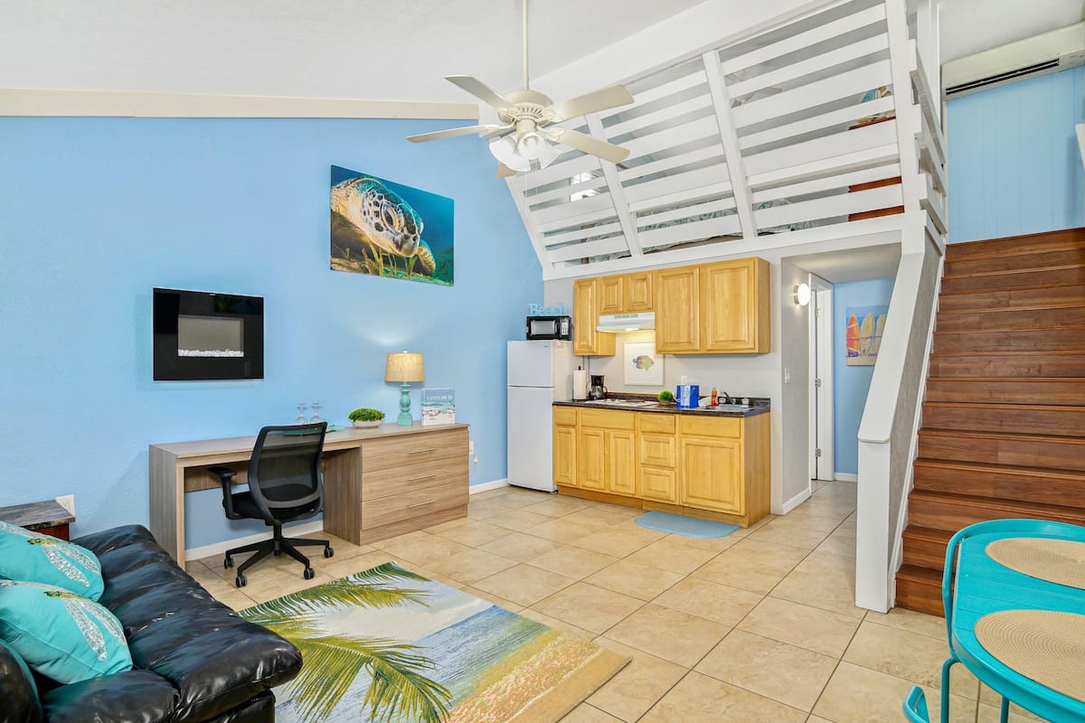 A compact living space with a kitchenette, a ceiling fan, a desk, and a sofa.