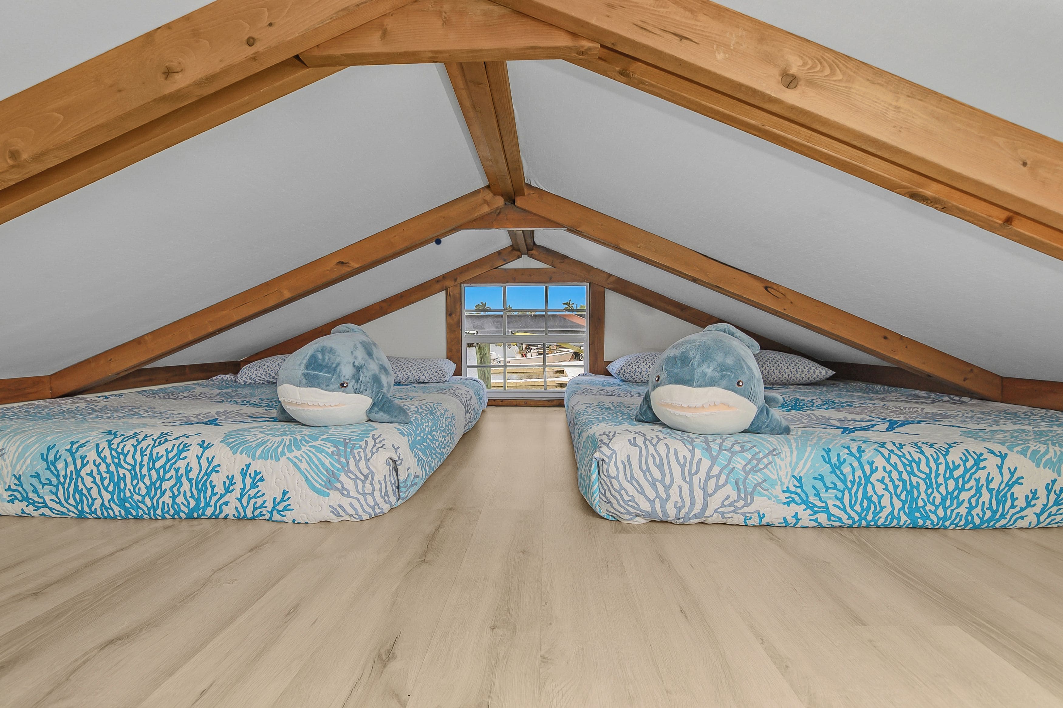 A bedroom with a sloped ceiling, two beds with ocean-themed bedding, and a window with a view of the outside.