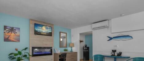 A hotel room with a bed, desk, chair, potted plant, and a wall-mounted TV.