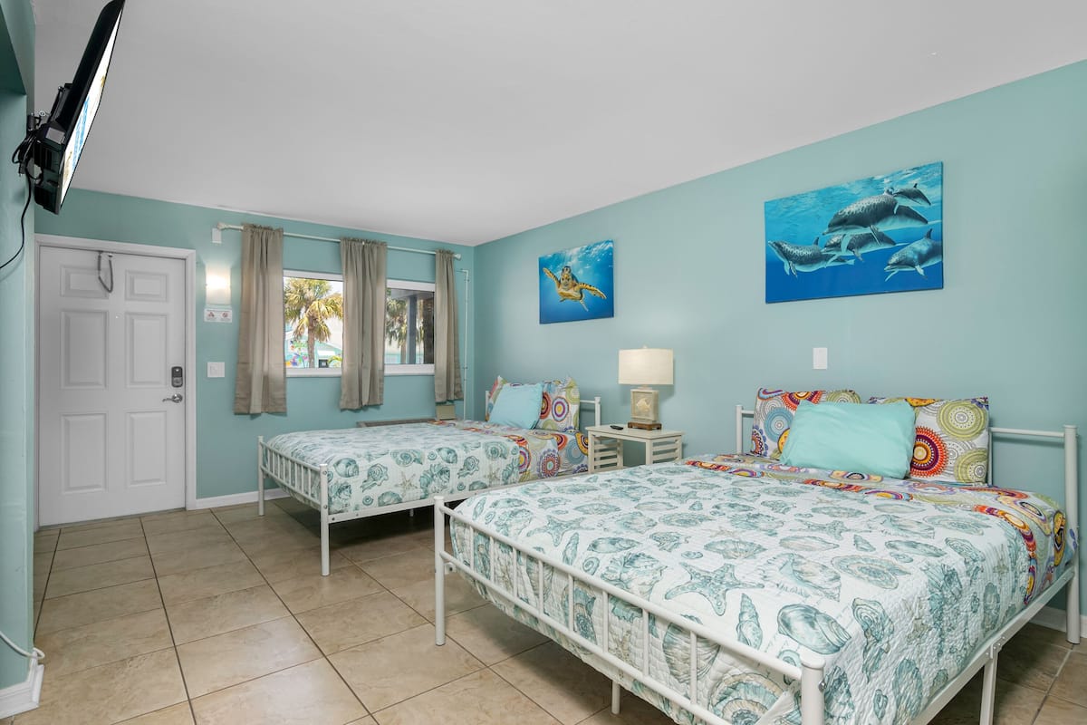 A room with two beds, a window with curtains, a door, and two wall-mounted paintings.