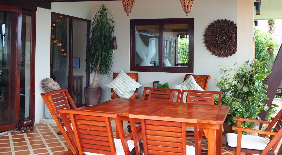 A wooden dining table with six chairs, surrounded by potted plants and a large mirror.