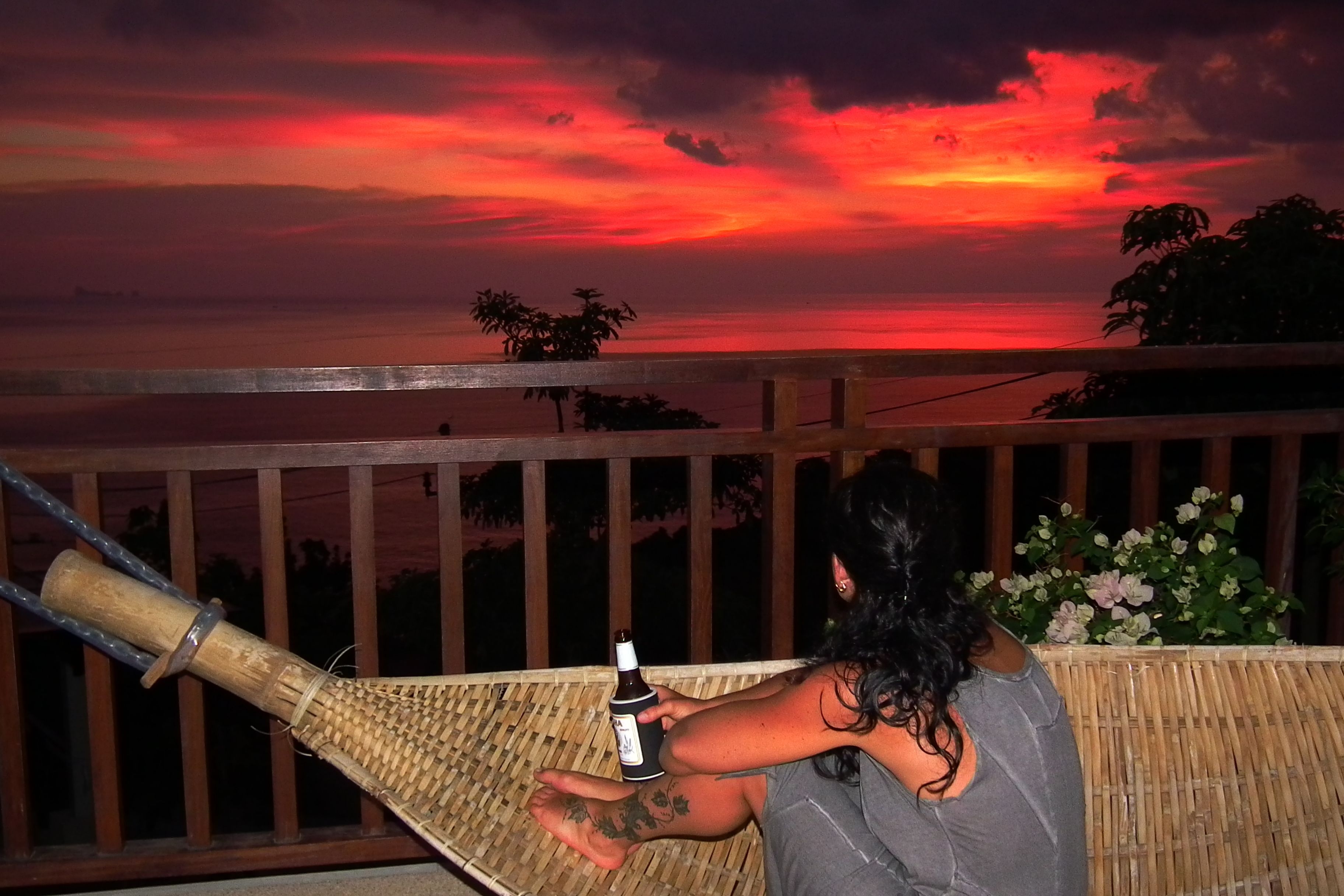 A person holding a bottle on a balcony with a sunset view.