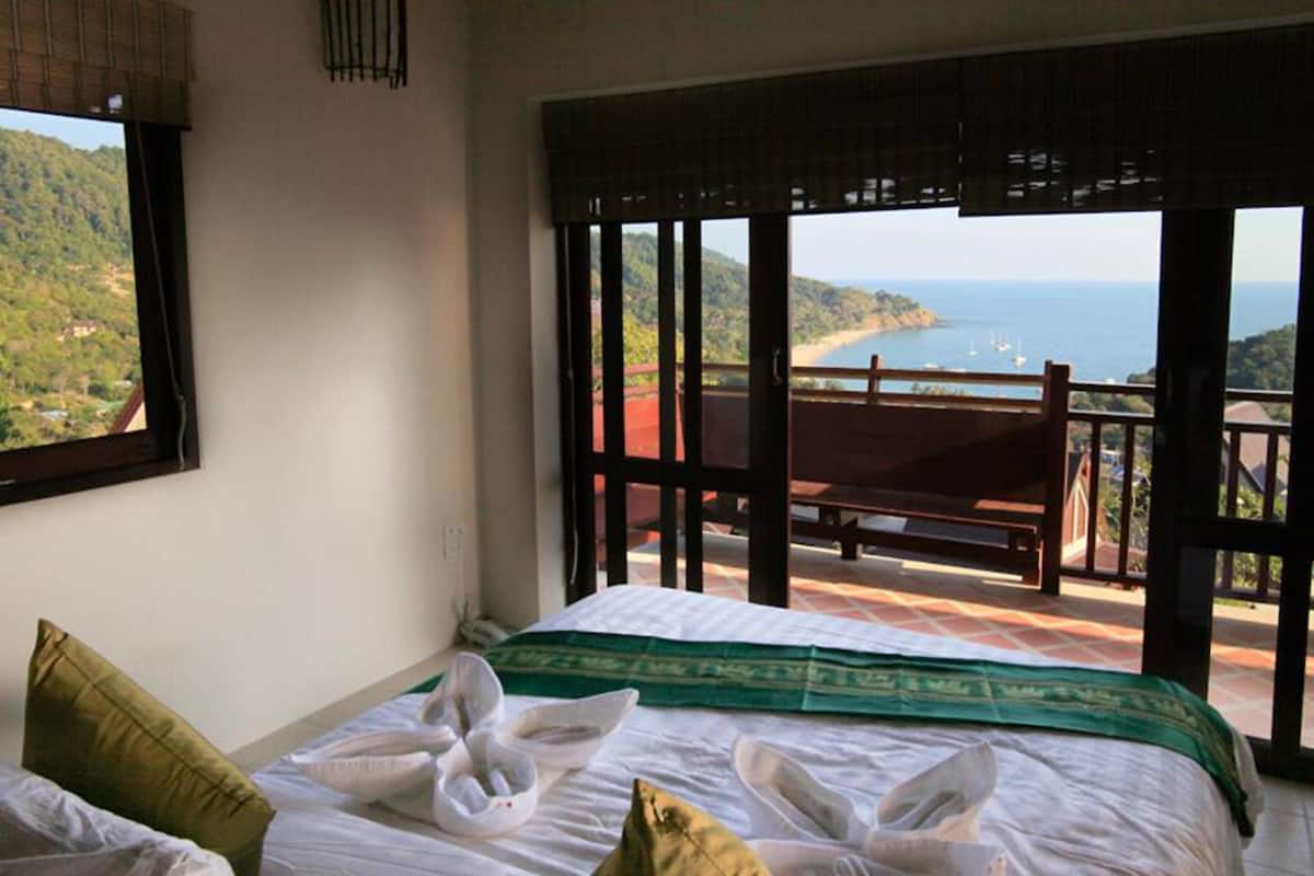 Un dormitorio con cama, almohadas y vistas al mar a través de amplios ventanales.