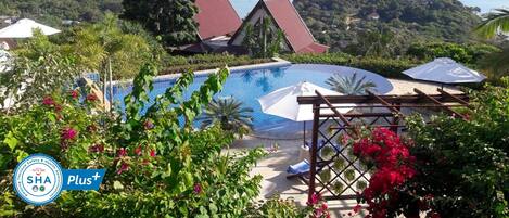 Una piscina con vistas al mar, rodeada de vegetación y una casa con tejado rojo.