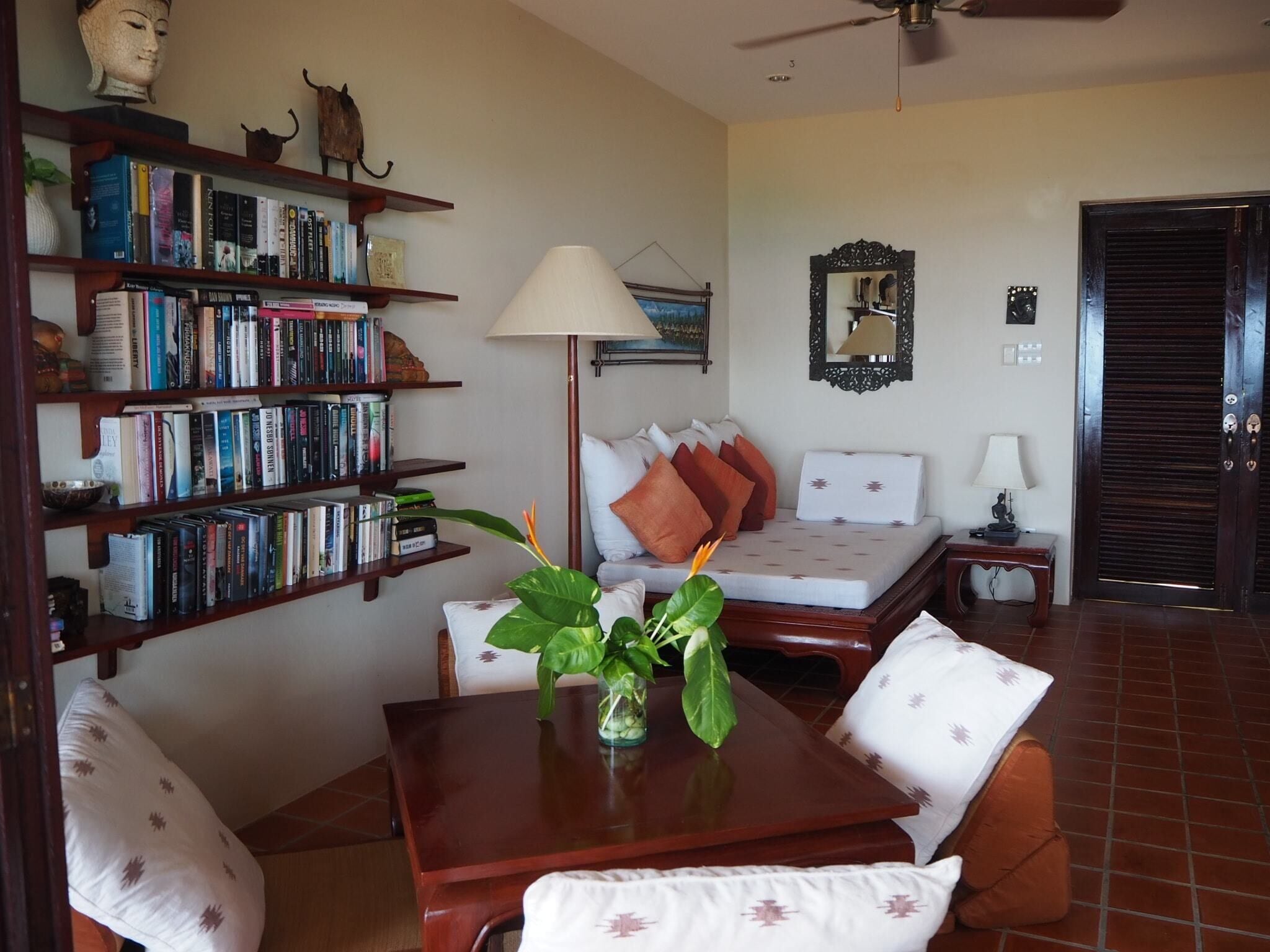 A well-lit room with a bed, a bookshelf, a table with a plant, and a ceiling fan.
