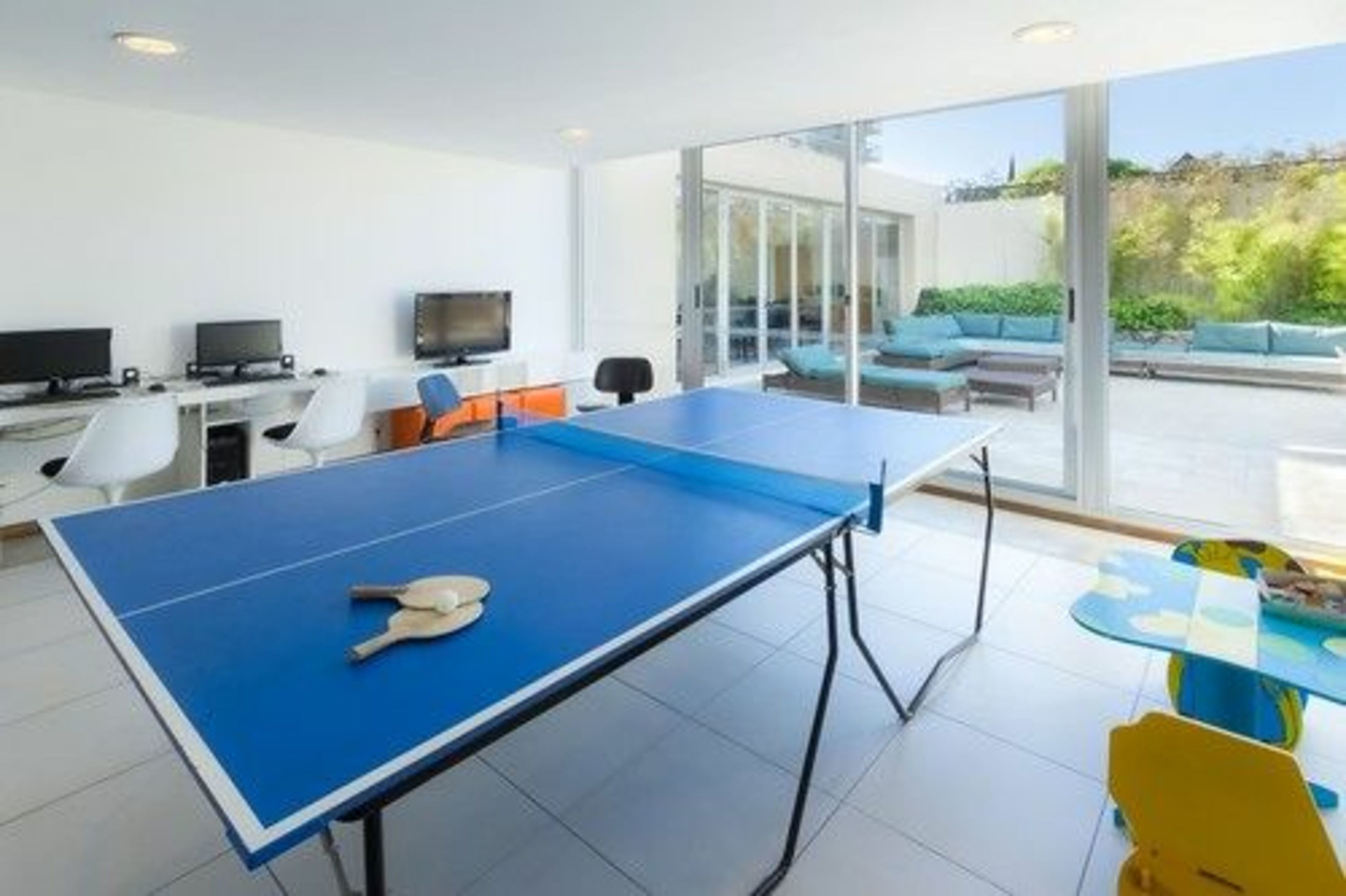 Habitació moderna amb taula de ping-pong, televisió i sofà amb vistes a l'exterior.