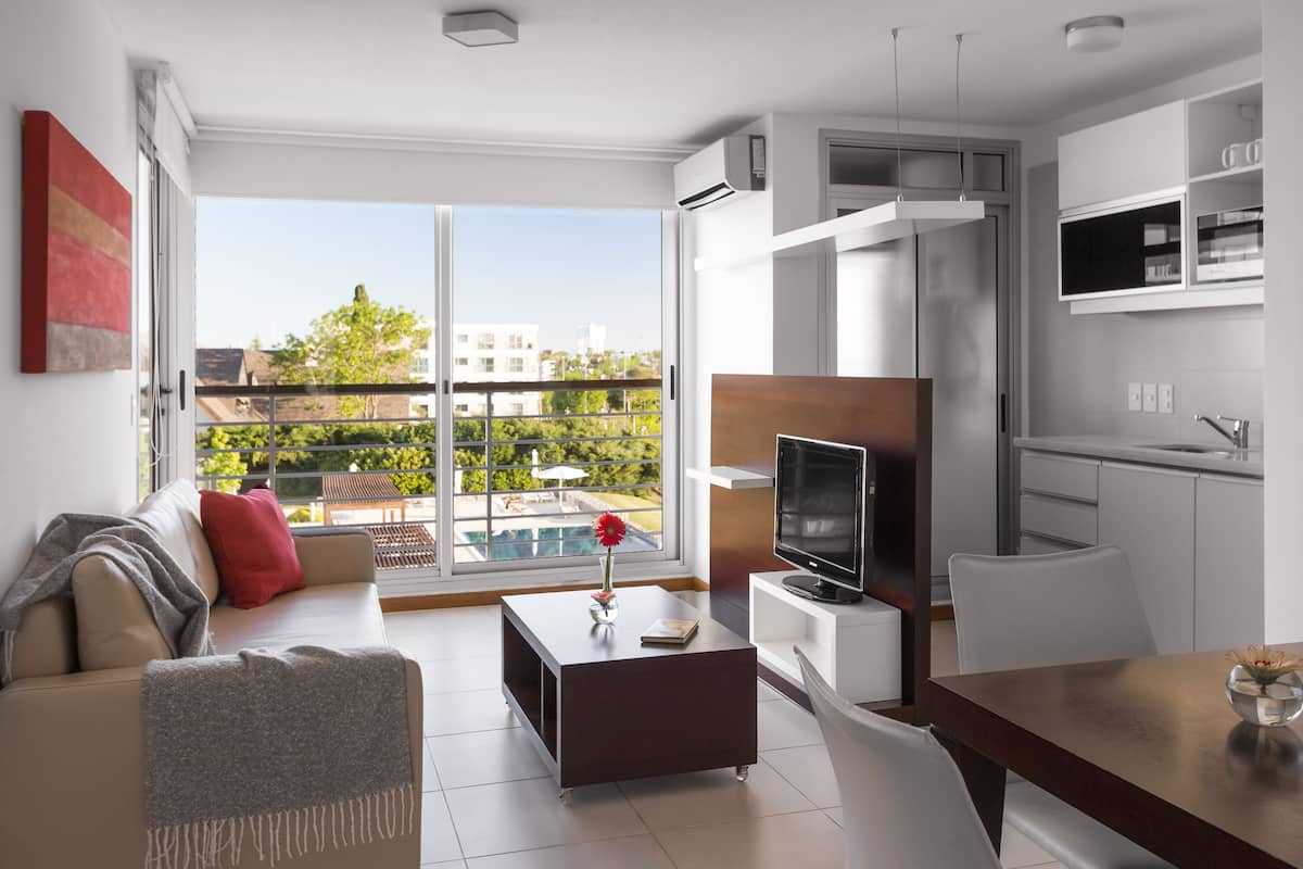 Un apartamento moderno con balcón, zona de comedor y sala de estar con televisor.