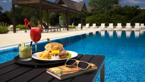 A poolside table with a meal, a drink, and sunglasses. - Real Colonia Hotel & Suites (Colonia del Sacramento)