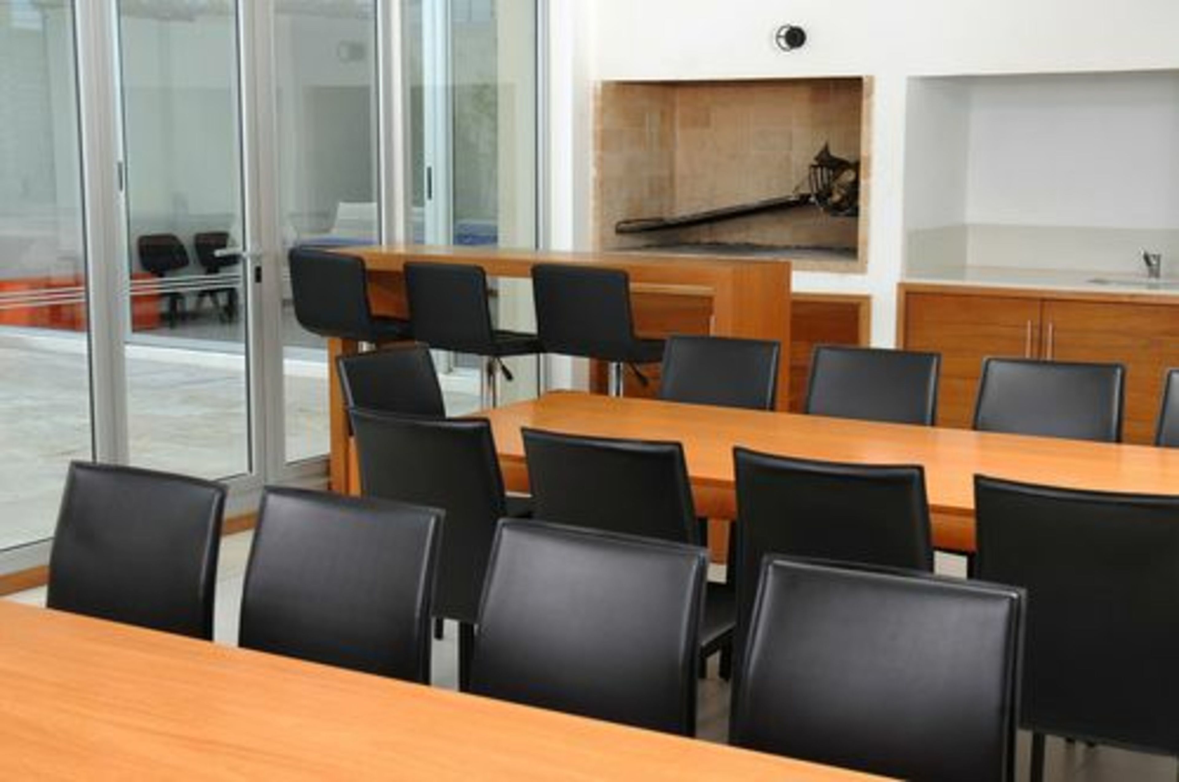 Konferenssihuone, jossa on pitkä pöytä ja mustat tuolit, lasiseinä, josta on näkymä, sekä puinen kaappi, jossa on kuva.