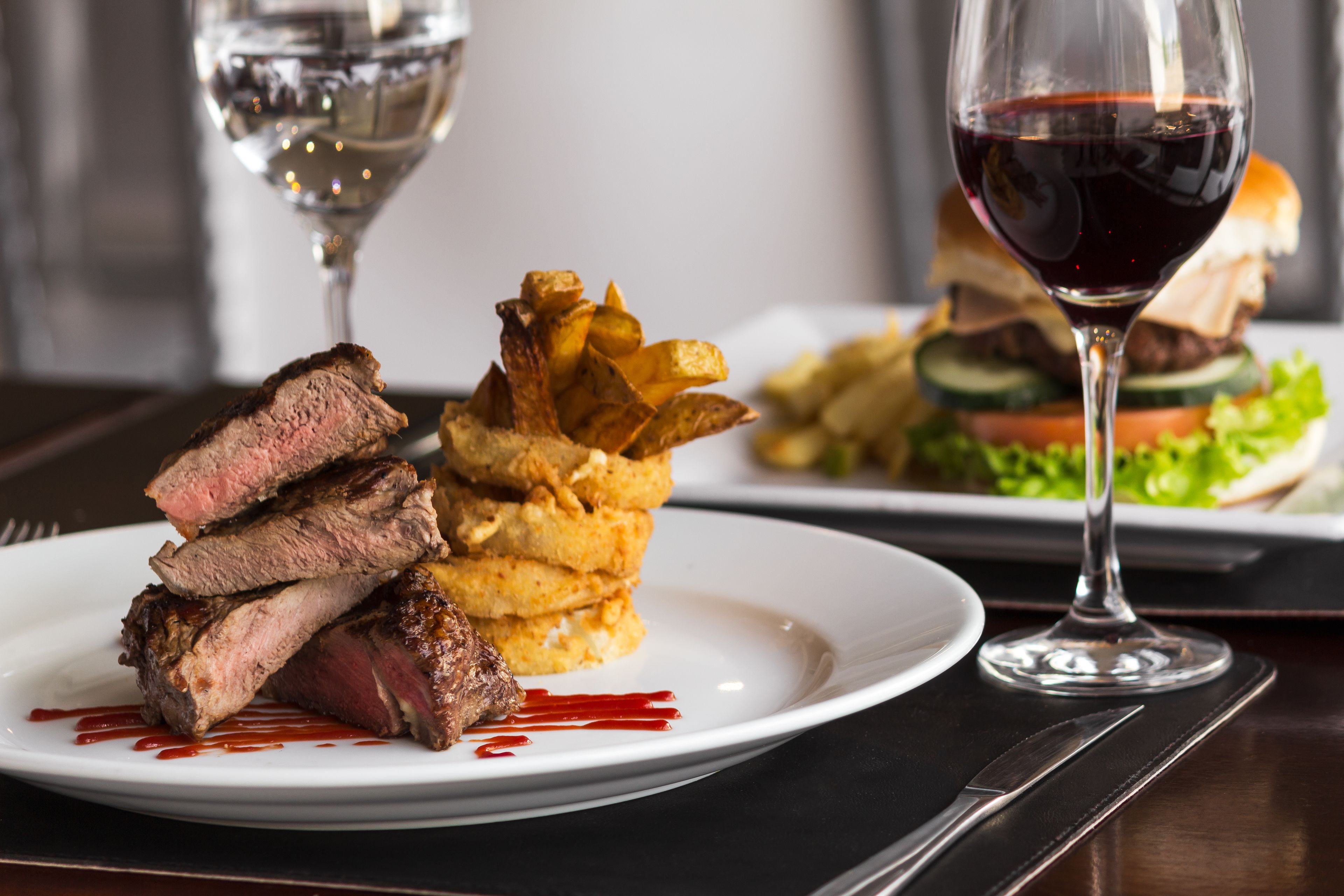 A plate of steak with fries and a glass of red wine on a table.