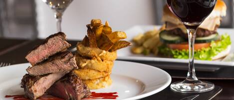 A plate of steak with fries and a glass of red wine on a table.