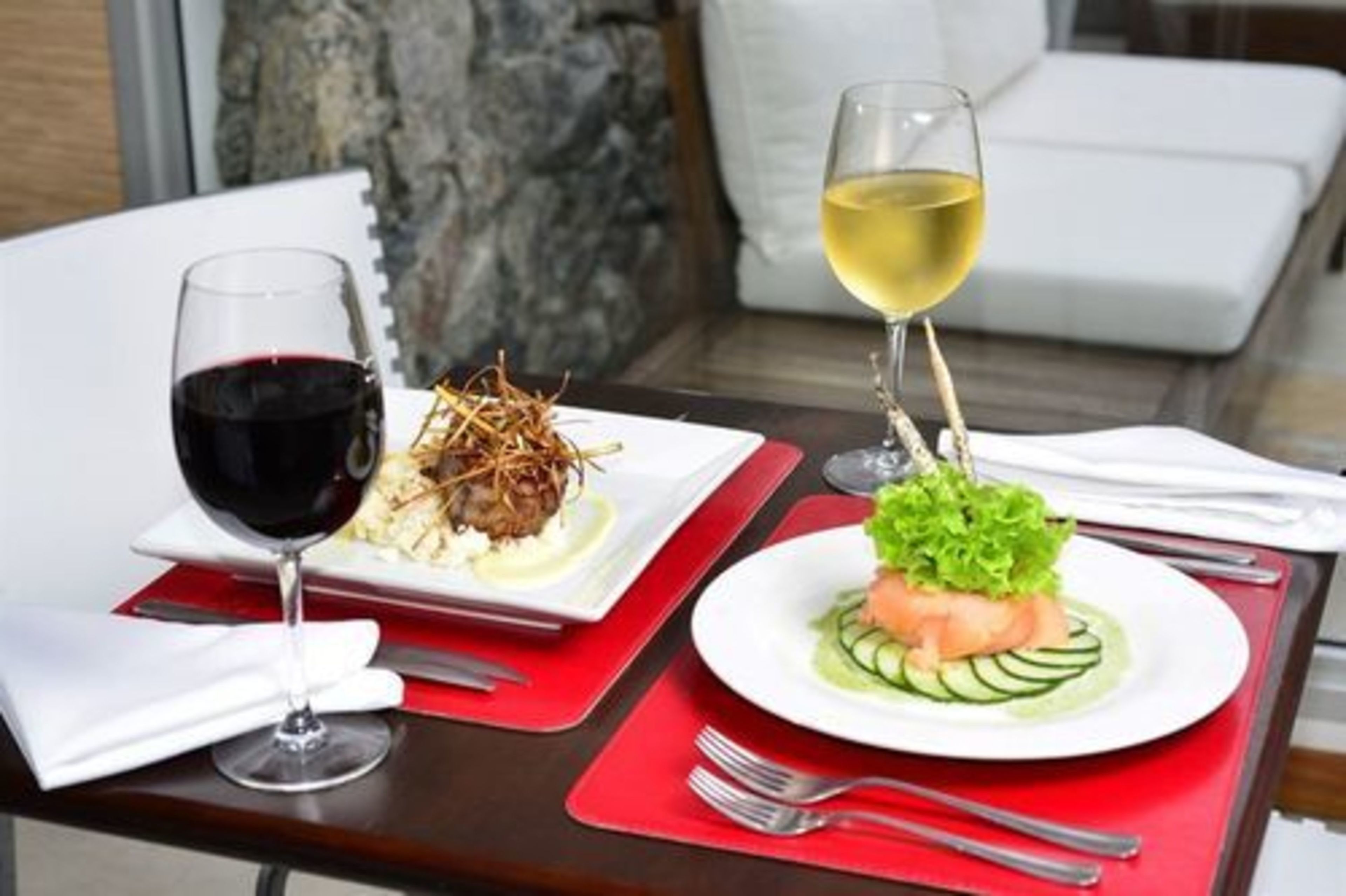 A dining table with two plates of food, a glass of red wine, and a glass of white wine.