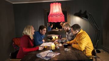 Een groep mensen zit rond een houten tafel in een kamer met donkere wanden en een rode hanglamp.