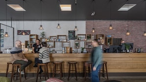 A bar area with wooden stools, a counter with shelves of bottles, and a brick wall.