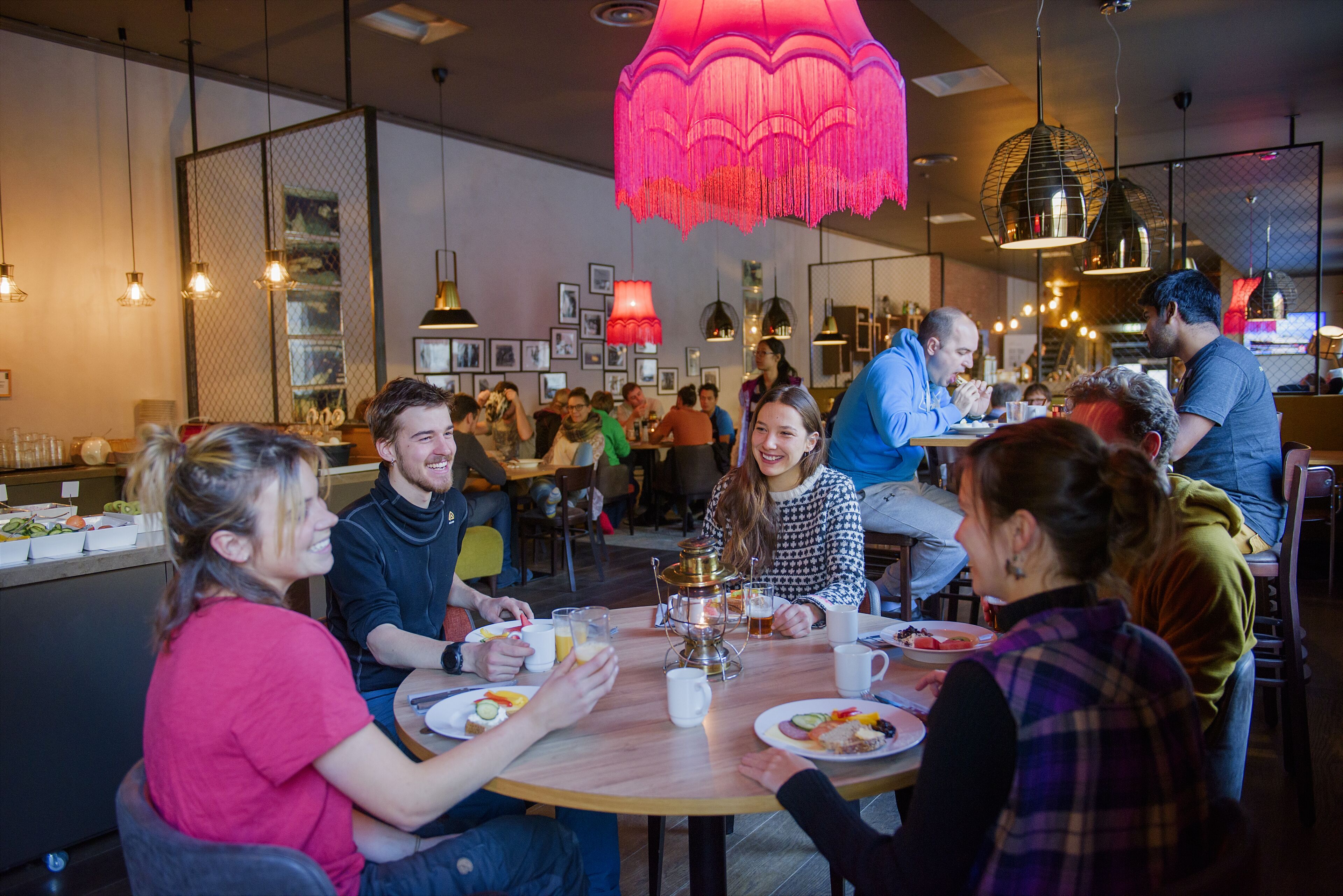 A group of people dining at a restaurant with a round table, pendant lights, and a decorative hanging light fixture.
