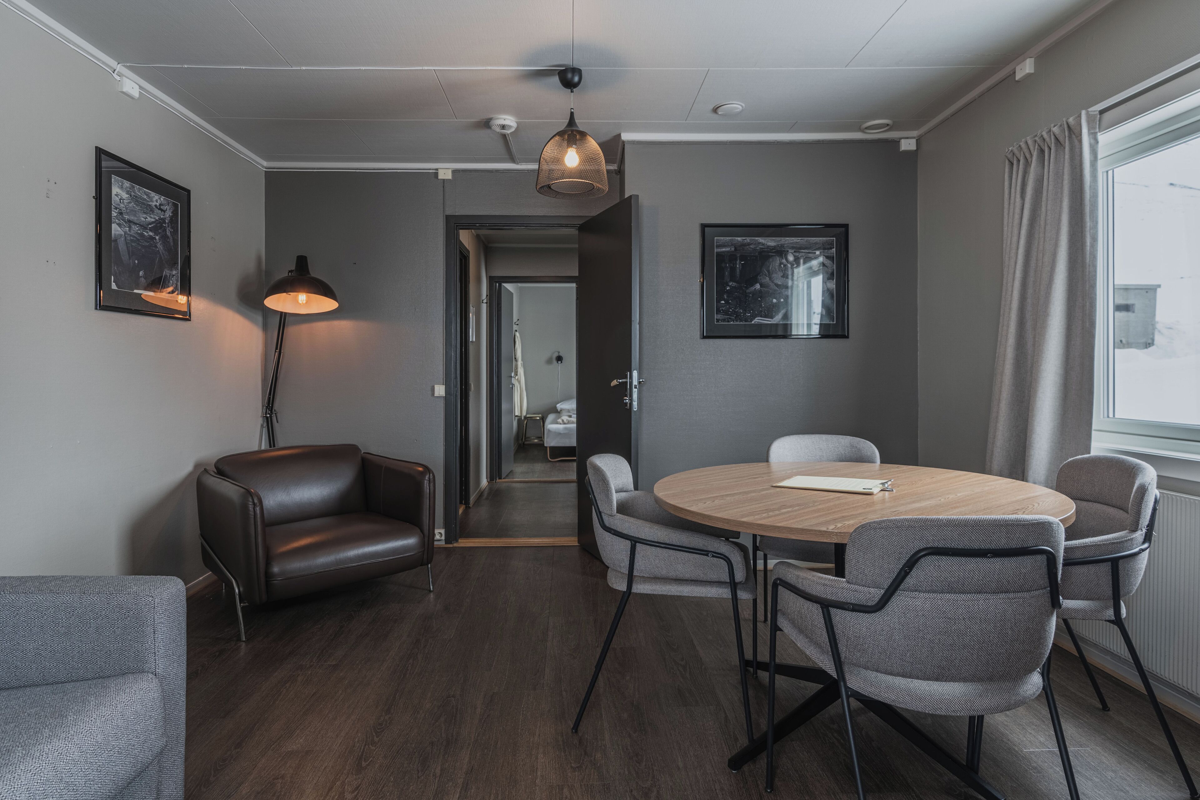 A modern room with a round table, leather chairs, a standing lamp, and framed pictures on the walls.