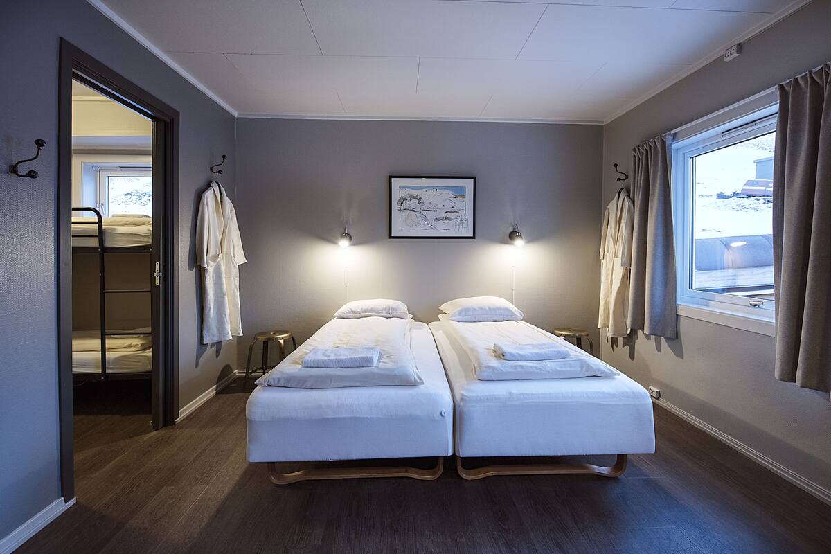 A hotel room with two single beds, a framed picture on the wall, and a window with curtains.