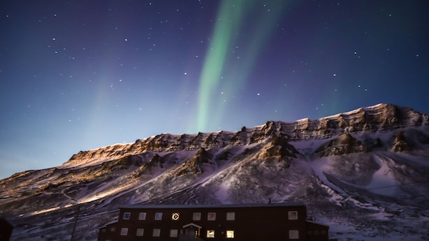 A building with multiple windows and a snow-covered landscape under a starry night sky with visible aurora borealis.
