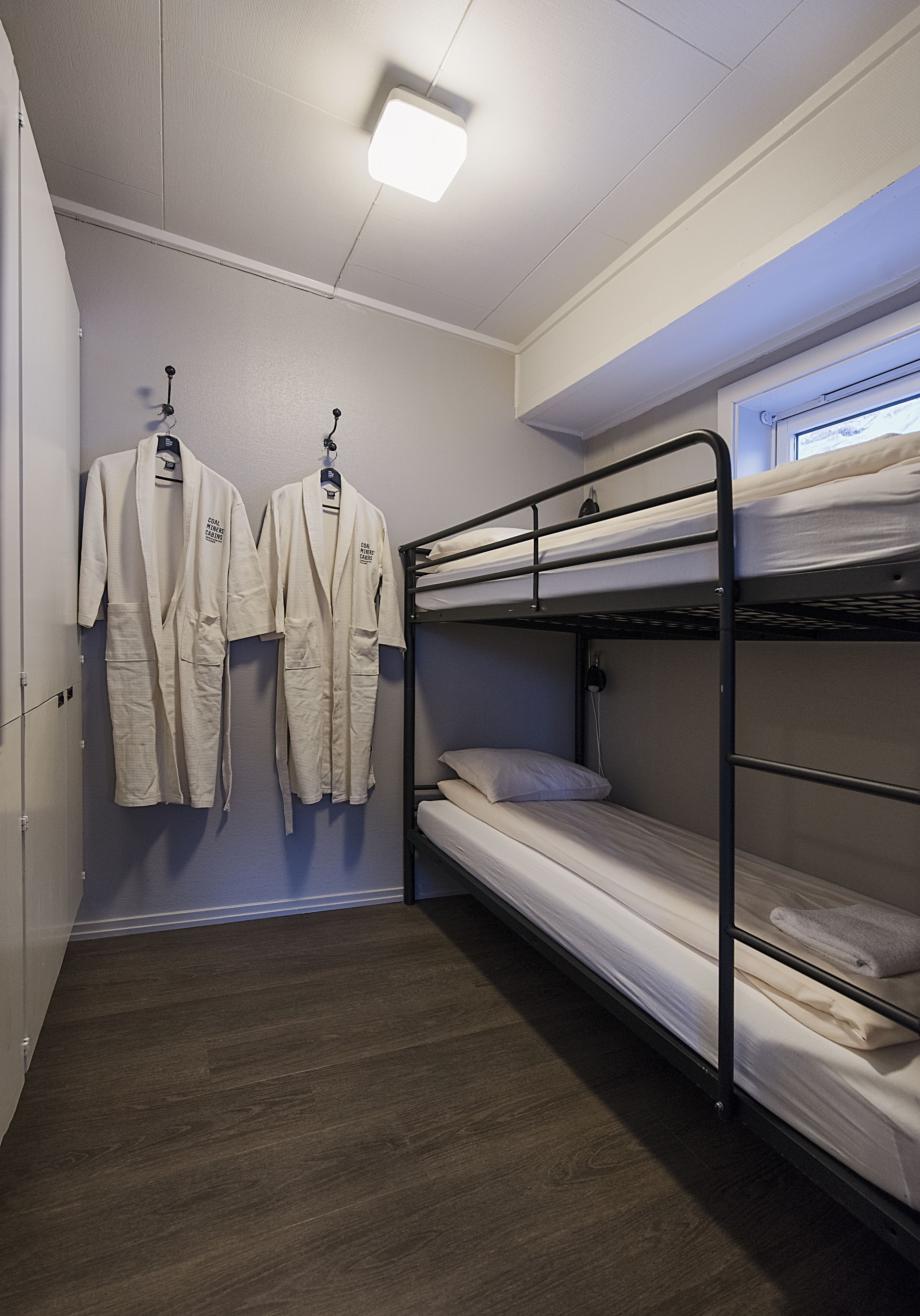 Ein Zimmer mit Etagenbetten, einem Kleiderschrank und zwei Kleidungsaccessoires, die an Haken hängen.