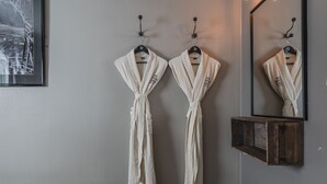 Two white robes hanging on hooks against a wall with a mirror below them.